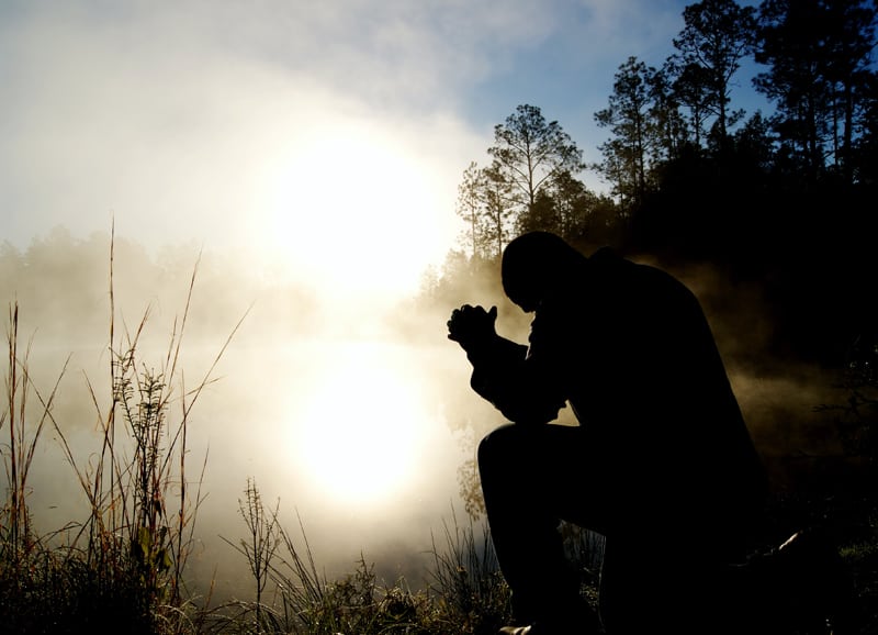man kneeling on one knee in prayer at sunrise